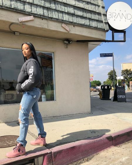 Draya Michele in a blue jeans poses for a picture in front of a house.